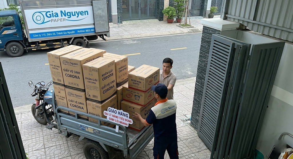Một nh&acirc;n vi&ecirc;n giao h&agrave;ng dỡ c&aacute;c th&ugrave;ng h&agrave;ng khăn giấy Gia Nguyễn Paper từ xe m&aacute;y v&agrave;o một cửa h&agrave;ng tạp h&oacute;a nhỏ, với bảng hiệu 'Sinh lời nhanh'